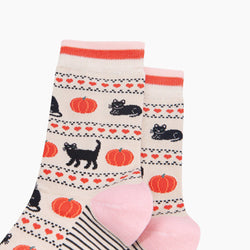 A pair of crew socks with a cozy autumn pattern featuring black cats, orange pumpkins, and red hearts on a cream background