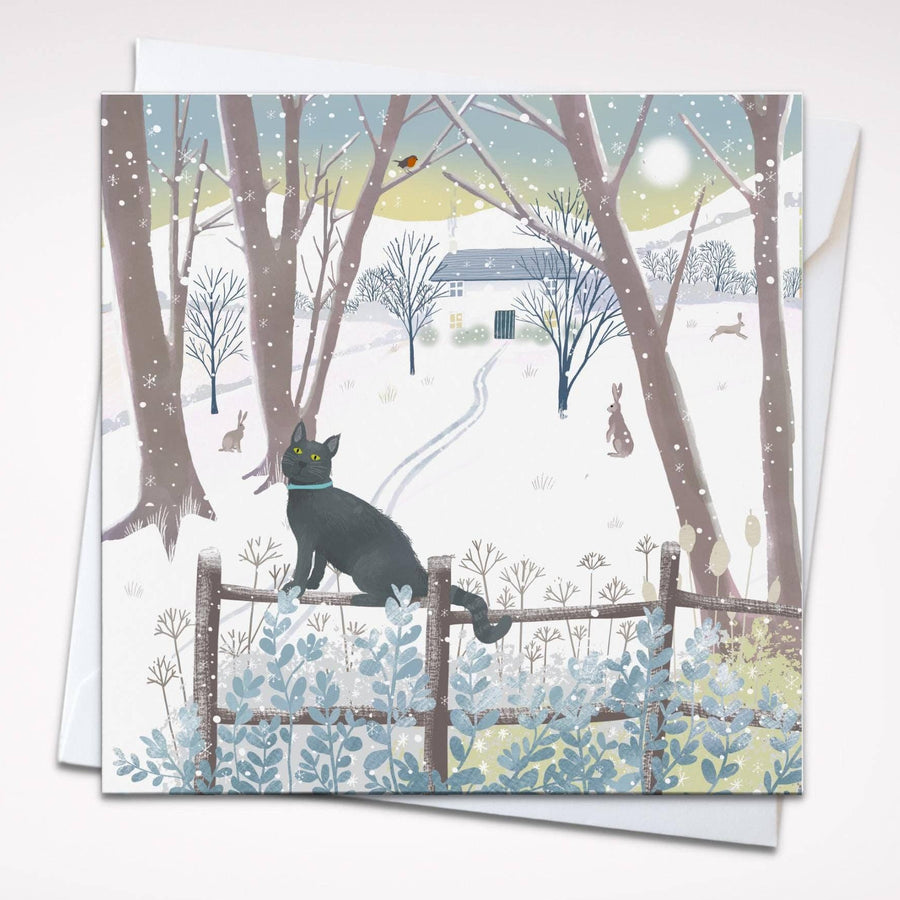 A square card featuring a winter landscape with a black cat sitting on a fence, surrounded by snow, bare trees, and a small house