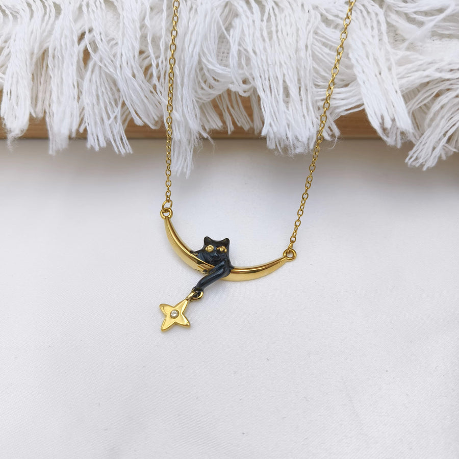 A gold chain necklace featuring a crescent moon pendant with a black cat figurine and a dangling gold star charm