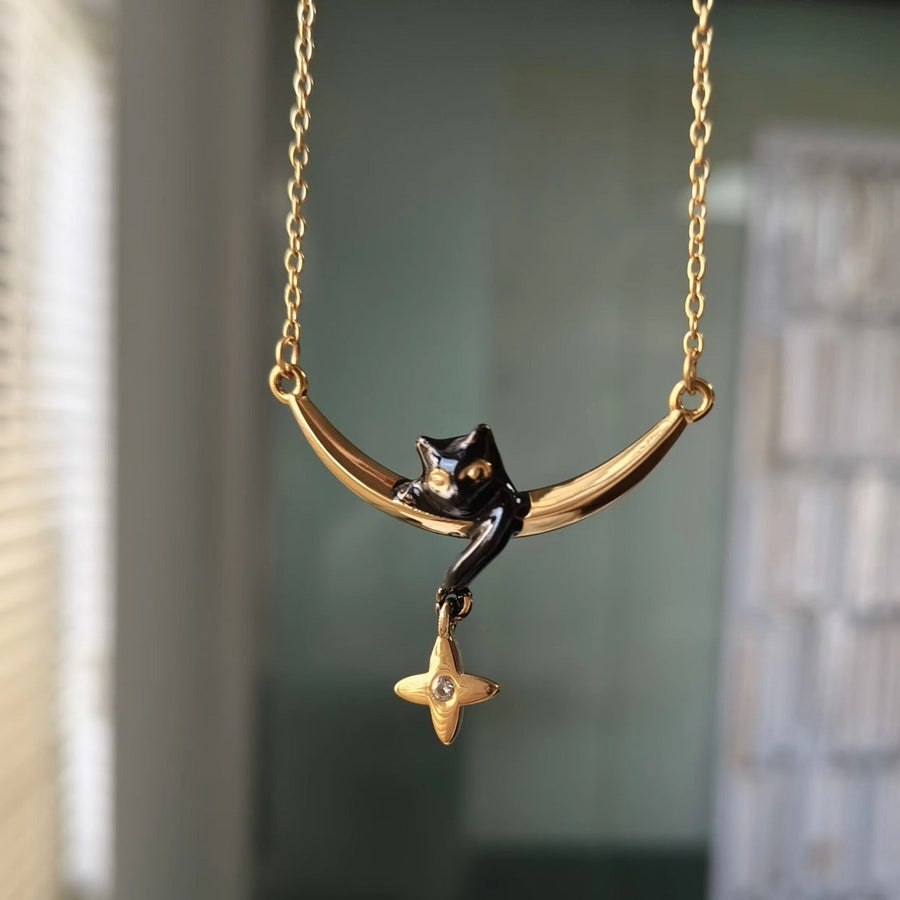 A gold crescent moon necklace with a black cat figurine and a dangling gold star charm