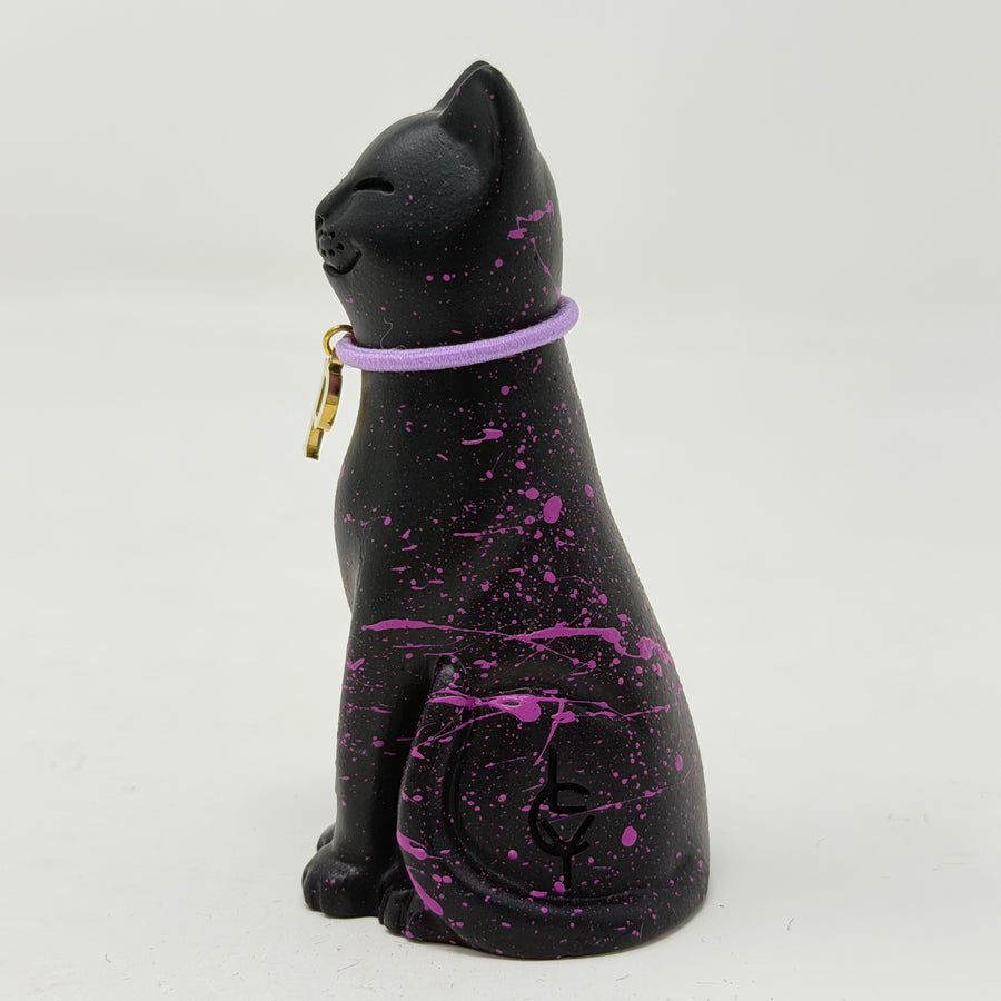 A black lucky cat figurine with purple paint splatters and a purple collar, shown against a plain light gray background.