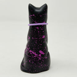 A black lucky Cat figurine with vibrant magenta splatter details and a matching purple collar, shown from the back against a plain white background.