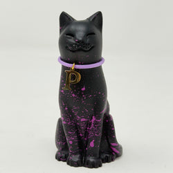 A black lucky cat figurine with purple paint splatters and a purple collar featuring a gold letter 'P' charm, set against a plain light gray background.
