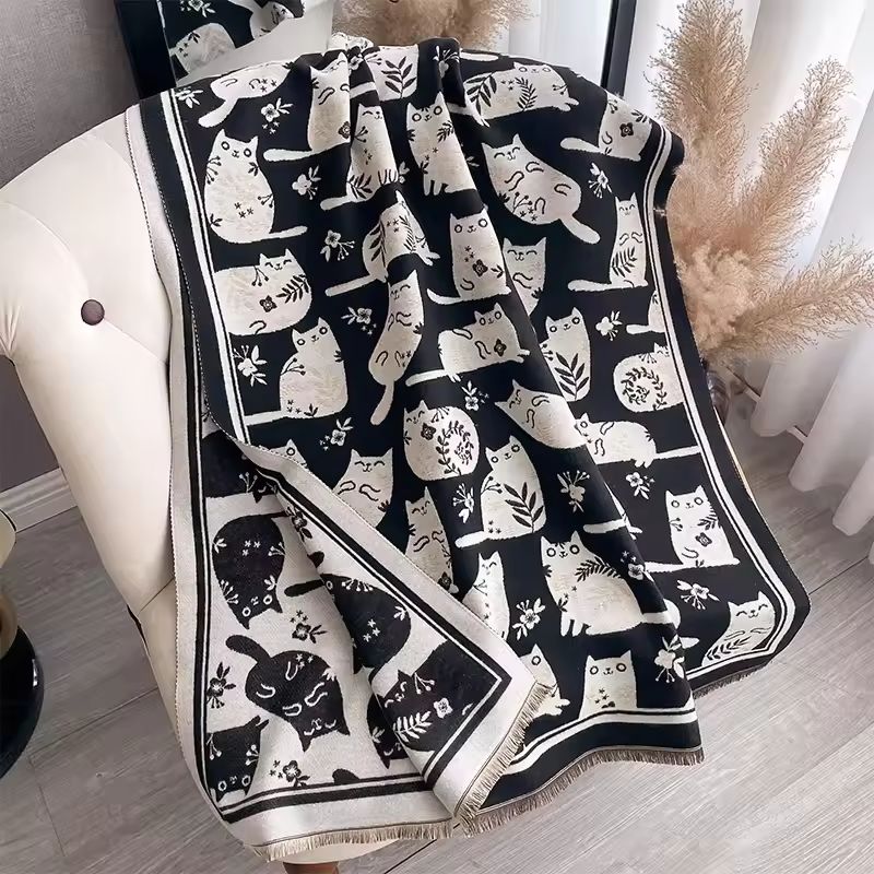 Black and white patterned fabric scarf with cat design draped over a chair. With fringe