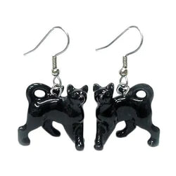 A pair of black porcelain earrings shaped like cats in a running pose, with surgical steel hooks