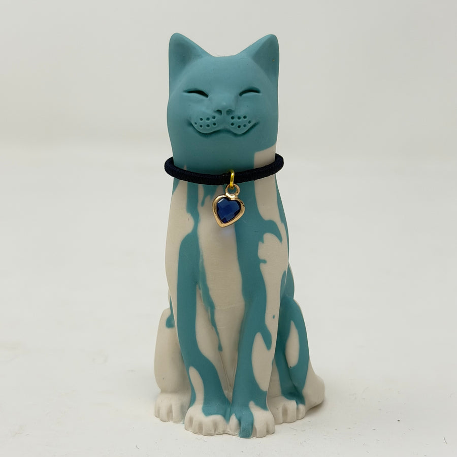 A resin cat figurine with a teal and white marbled pattern, wearing a black collar with a blue heart charm
