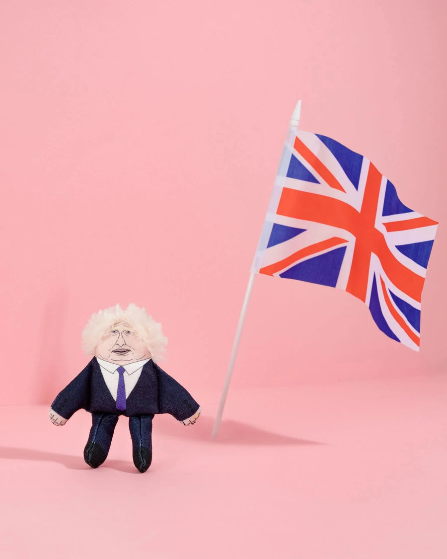 Small Boris Johnson look-a-like figure in a suit with a Union Jack flag against a pink background