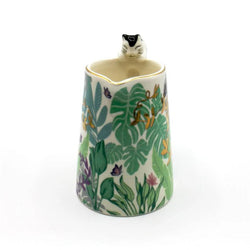 Decorative mug with a jungle leaf pattern and a cat figurine on a white background