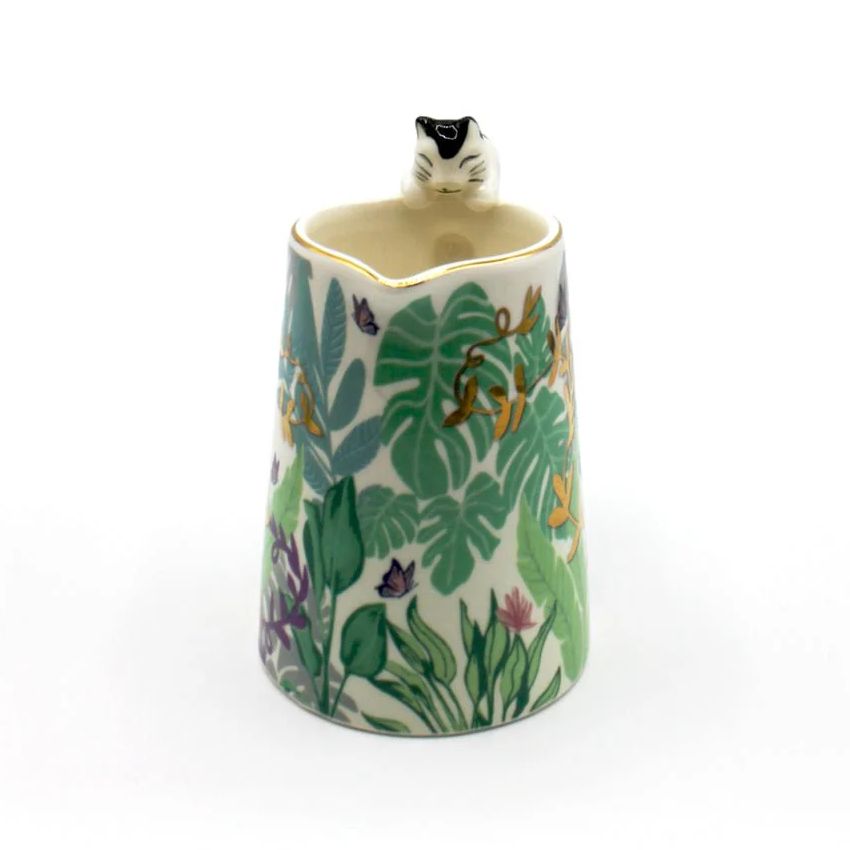 Decorative mug with a jungle leaf pattern and a cat figurine on a white background