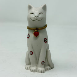 A white resin lucky cat figurine with a brown collar and a red heart charm, decorated with small red and white Yorkshire Rose patterns on its body, set against a plain light grey background.