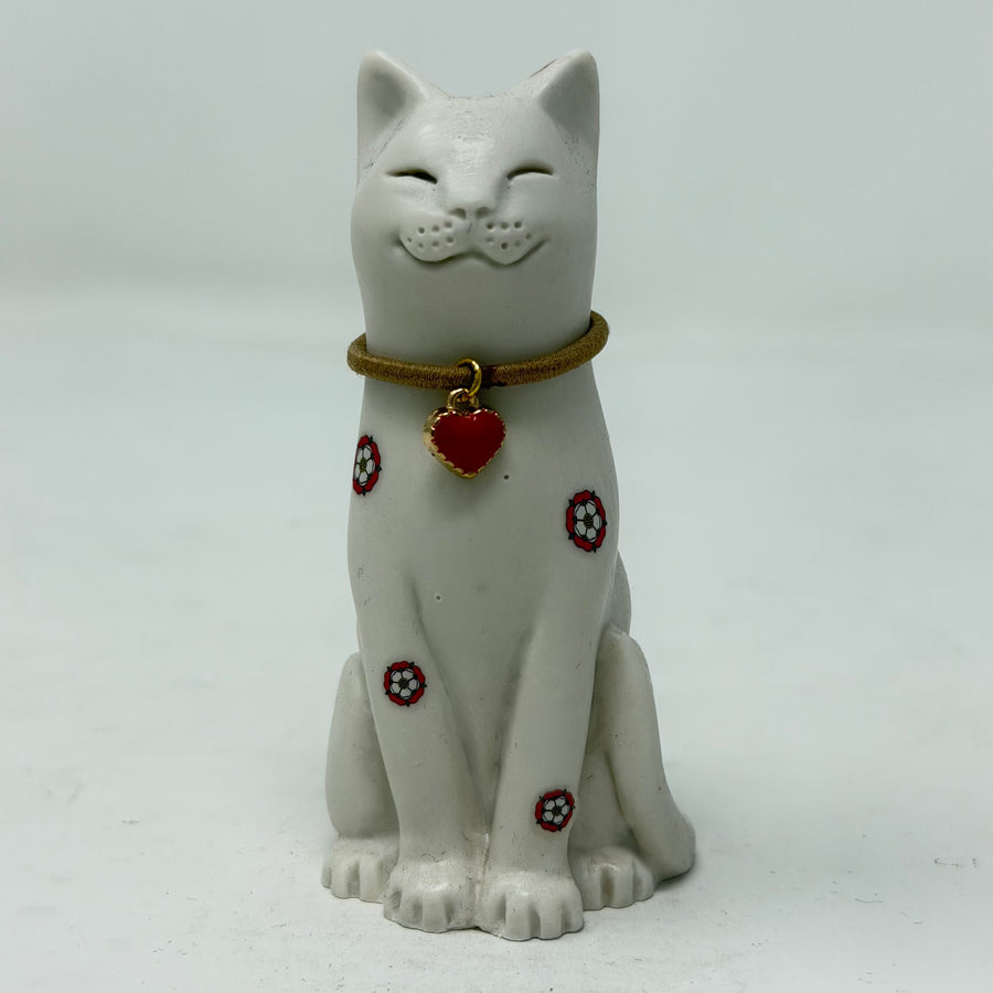 A white resin lucky cat figurine with a brown collar and a red heart charm, decorated with small red and white Yorkshire Rose patterns on its body, set against a plain light grey background.