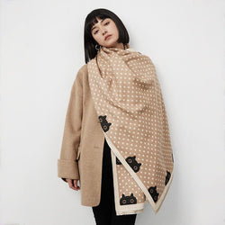 Woman wearing a beige shawl with black cat and polka dot patterns draped over her shoulders against a white background