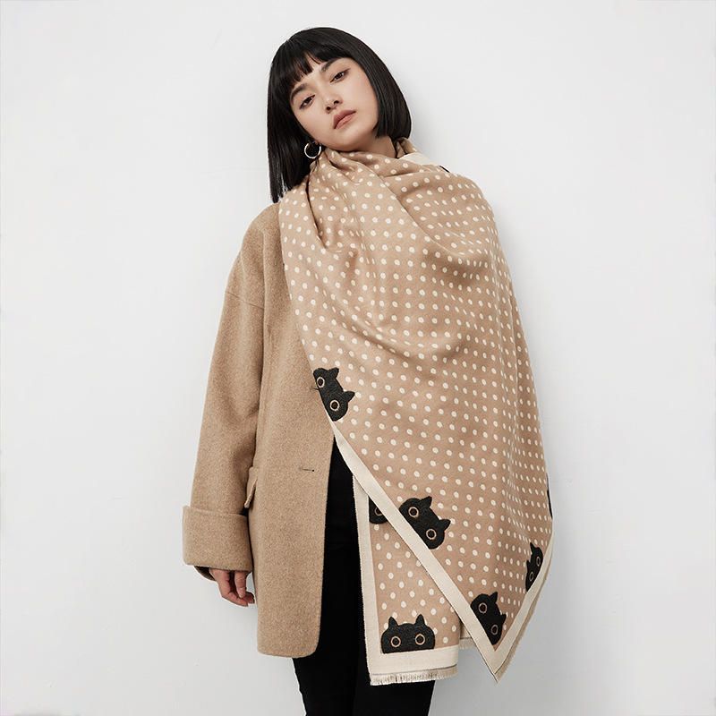 Woman wearing a beige shawl with black cat and polka dot patterns draped over her shoulders against a white background