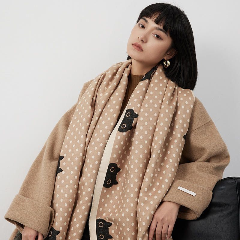 Woman wearing a beige coat with a black cat and polka dot shawl against a white background