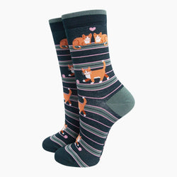 A pair of crew socks with a dark navy blue base, featuring horizontal stripes in pink, gray, and green, and decorated with cartoon orange tabby cats and small pink hearts