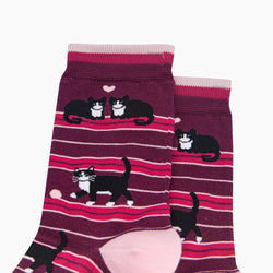 A pair of crew socks featuring a pattern of black and white cats on a berry red and pink striped background