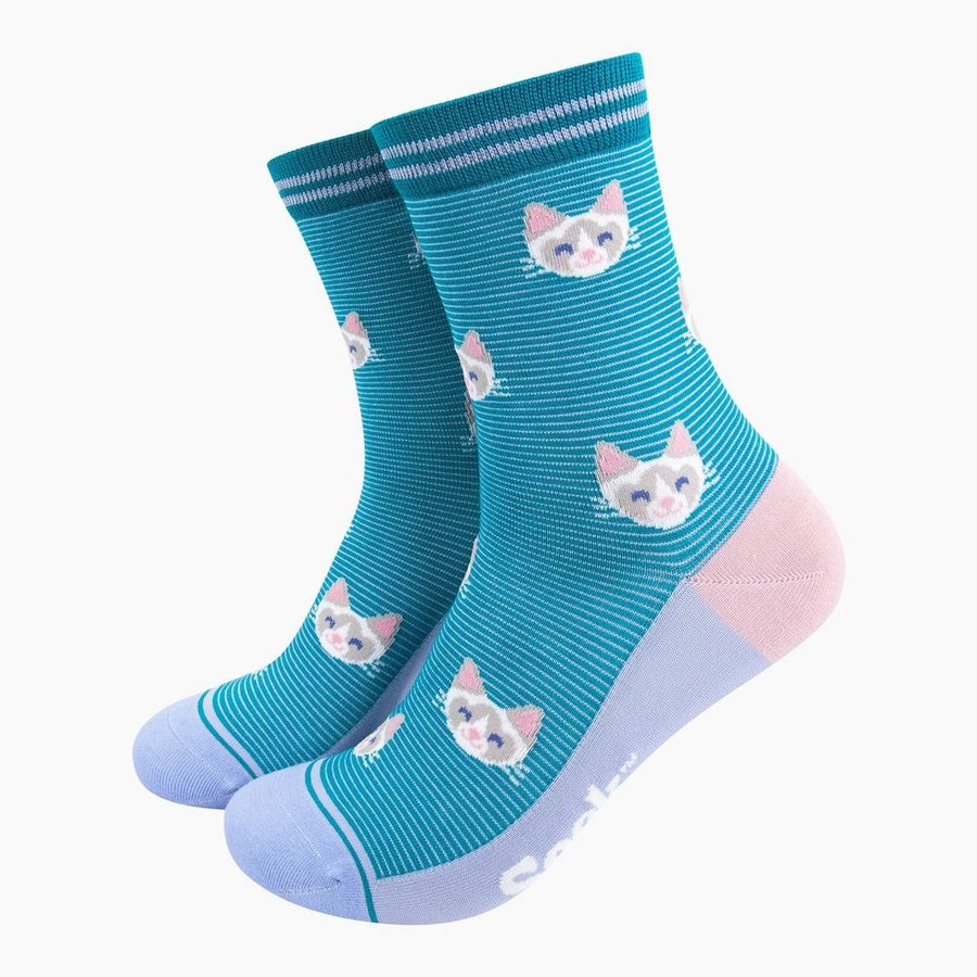 A pair of teal blue crew socks with thin white horizontal stripes, featuring a pattern of white and pink cat faces, light blue toes and heels, and a solid light pink heel section.