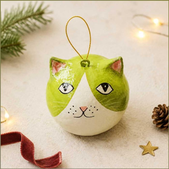 A round Christmas ornament shaped like a cat's face, with a glossy green and white design, pink inner ears, and a gold hanging loop