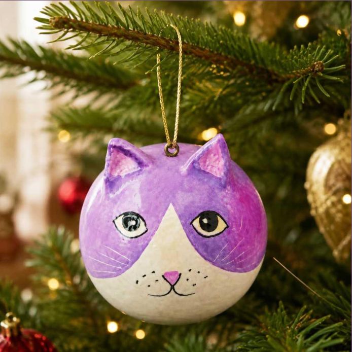 A round hand-painted Christmas ornament shaped like a cat's face, featuring purple and white coloring with black and gold details, hanging from a gold string