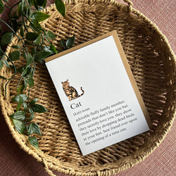 A printed card with a small cat illustration and a definition-style text block about a cat, placed on a woven straw tray