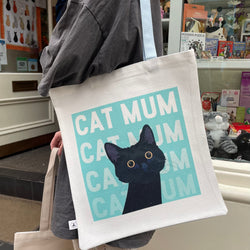 A person carrying a cream tote bag printed with Cat Mum and a Black Cat