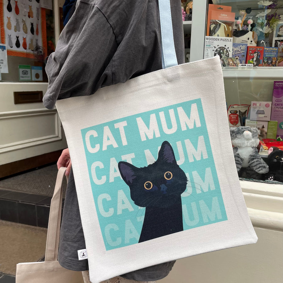 A person carrying a cream tote bag printed with Cat Mum and a Black Cat