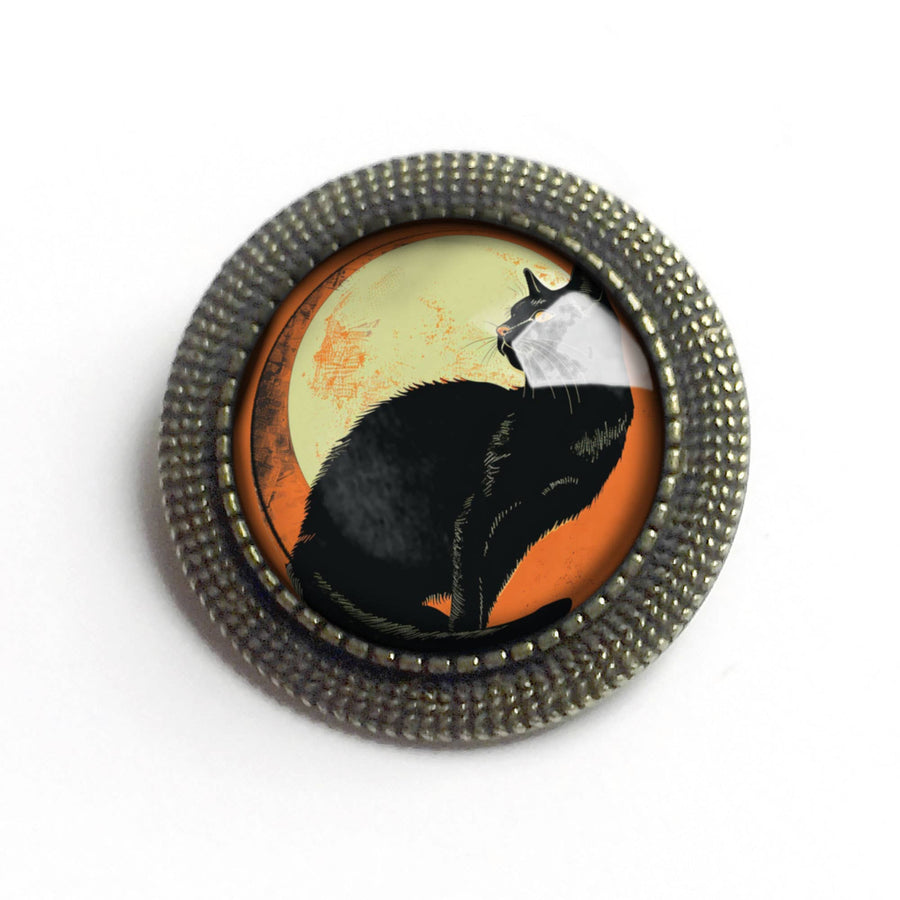 Round brooch with a black cat design on an orange background