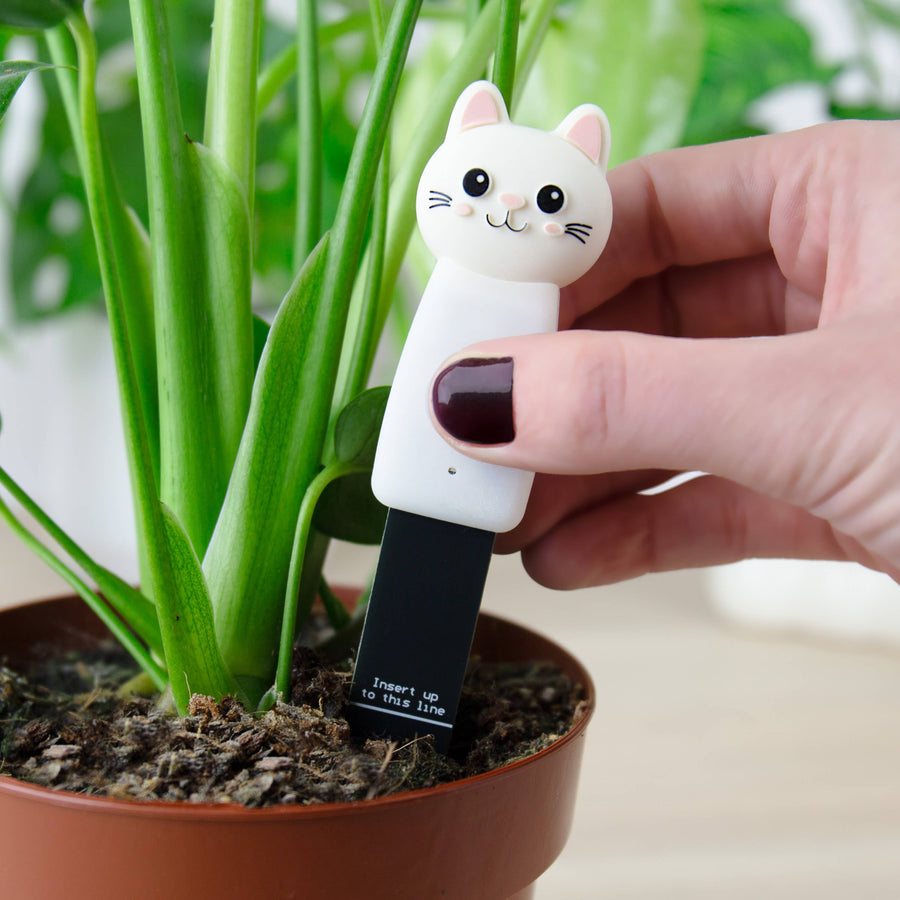 Hand holding a cat-shaped water indicator next to a potted plant