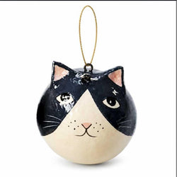 A round cat-face ornament with a glossy black and cream painted design, pink inner ears and nose, and a thin gold hanging loop at the top