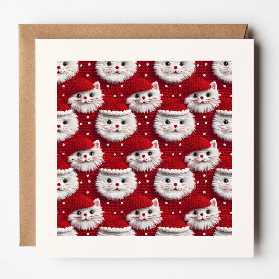 A square greeting card with a white border and kraft brown envelope, featuring a repeating pattern of white fluffy cat faces wearing red Santa hats on a red background.