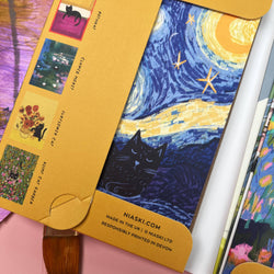 A close-up of a Van Gogh-inspired art print featuring a black cat under a swirling blue and yellow night sky