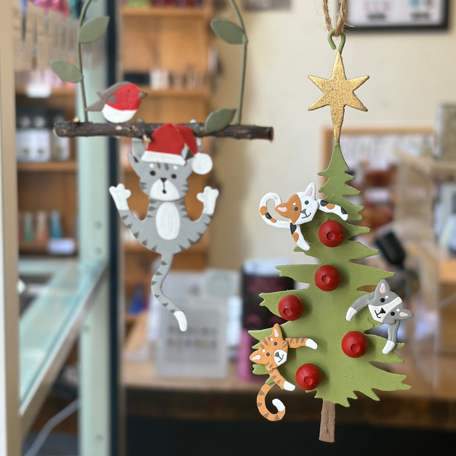 A hanging Christmas ornament featuring a green Christmas tree with red ornaments and small cat figures