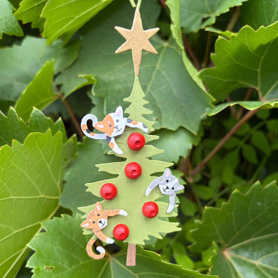 A metal Christmas tree ornament, decorated with small red beads, two orange-and-white cat figures, and a gold star topper
