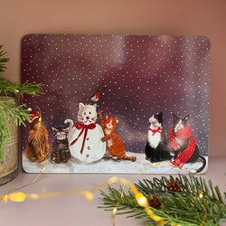 A rectangular placemat featuring five cats dressed in winter clothing, including a snowman, set against a snowy purple background. 