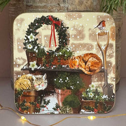 A square decorative coaster featuring a festive Christmas garden scene with a wreath, sleeping cats, flowers, a robin, and a shovel