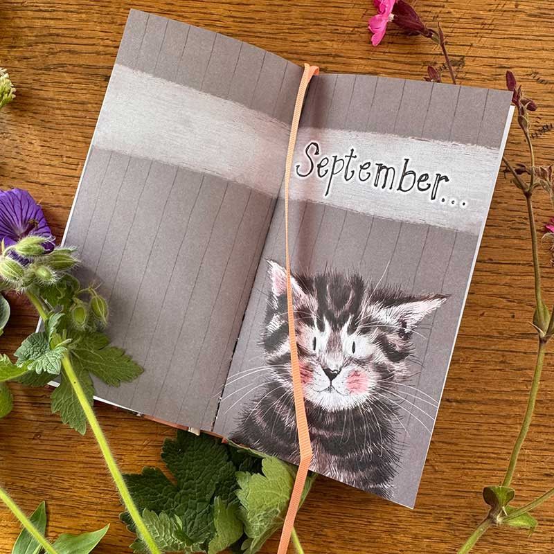 An open journal, with the left page showing grey lined paper and the right page featuring a Cat and the word 'September'.