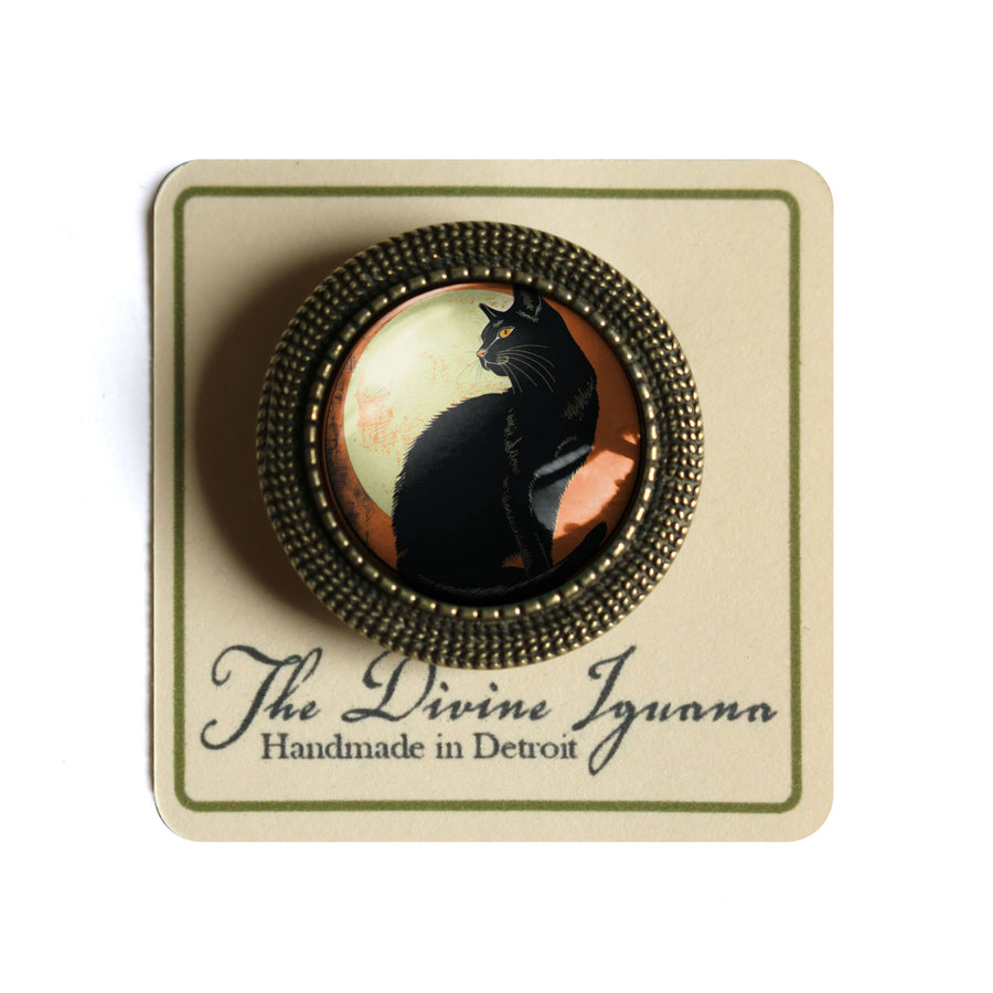 Black cat brooch on a card with 'The Divine Iguana' branding