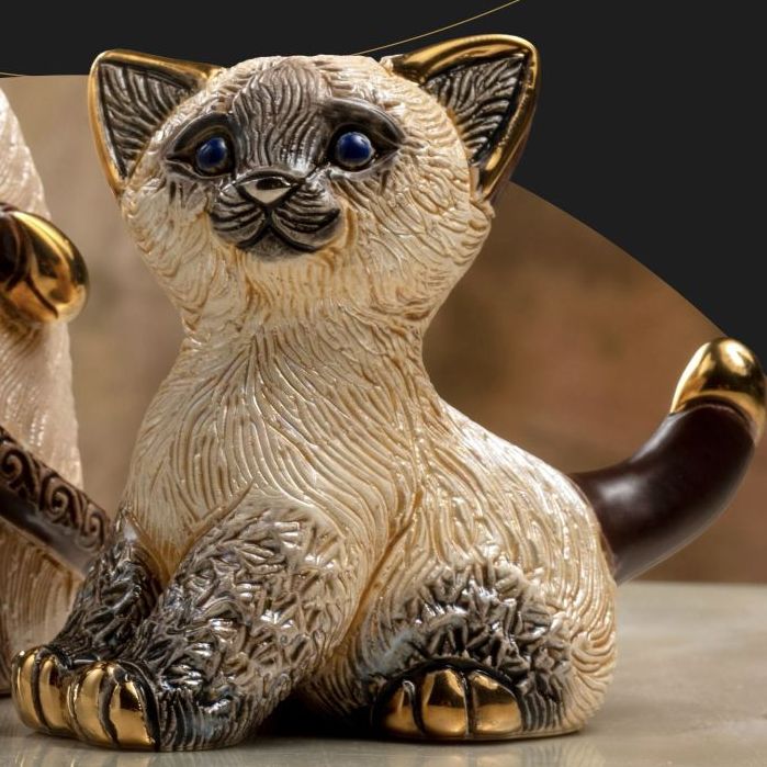 A decorative Chocolate point cat figurine with cream-coloured fur, dark brown patches on the ears, paws, and tail, and shiny gold accents