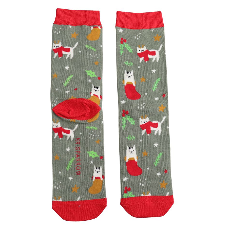 A khaki green pair of socks with red toes and ankle detailing. Adorned with white cats wearing red scarves, against mistletoe and stars background. 