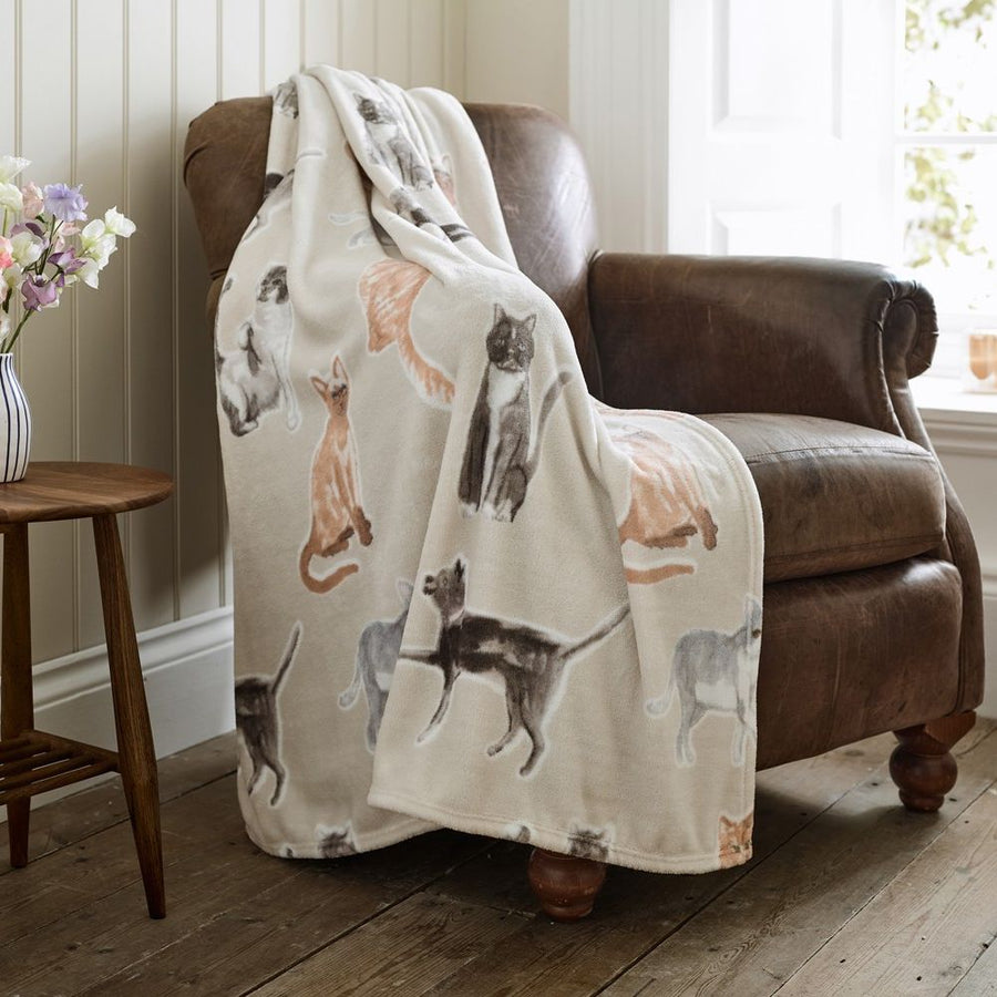 Blanket with cat pattern draped over a brown armchair in a room with wooden floor and window.