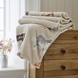 Folded blanket with cat pattern on a wooden dresser next to a window with flowers.