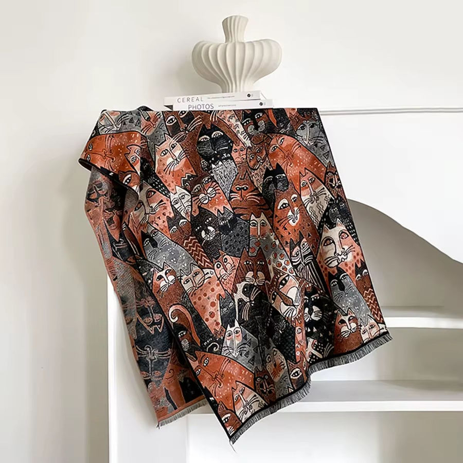 Decorative throw blanket with cat pattern draped over a chair against a white wall.