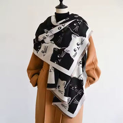 A reversible scarf with a black and white cat design displayed on a mannequin wearing a beige coat