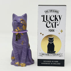 A purple lucky cat ornament with gold foil accents and lilac collar with P charm next to its retail packaging box labelled The Original Lucky Cat York