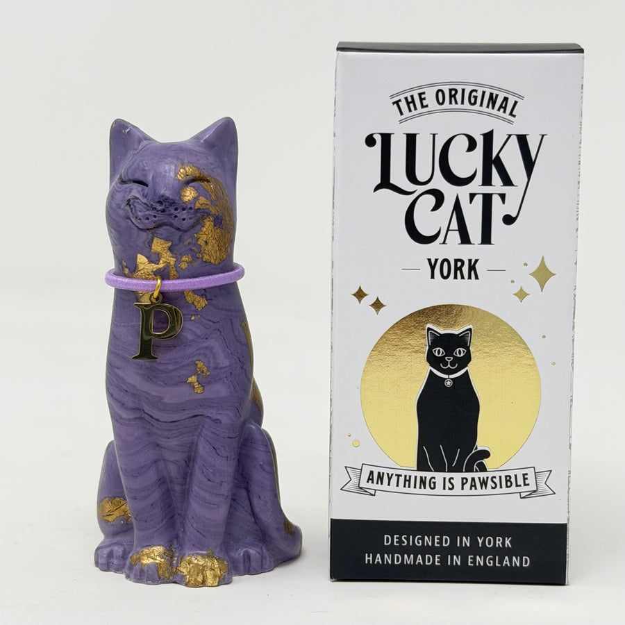 A purple lucky cat ornament with gold foil accents and lilac collar with P charm next to its retail packaging box labelled The Original Lucky Cat York
