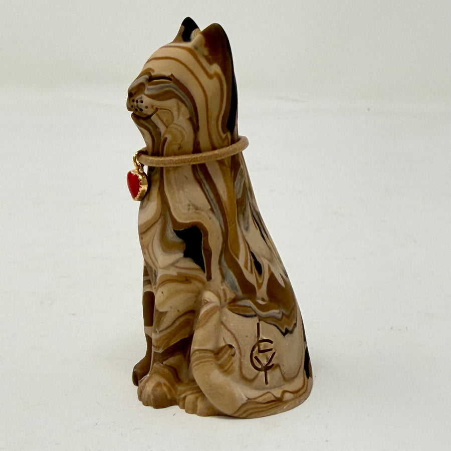 A marbled cream brown and black tabby Lucky Cat figurine wearing a brown collar with a red heart charm. Side view.