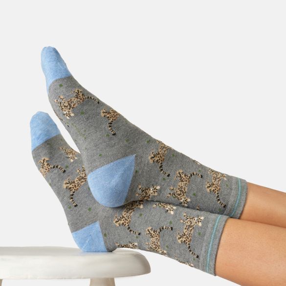 A pair of grey crew socks with light blue heels, toes, and soles, featuring a pattern of bengal cats worn on feet resting on a stool