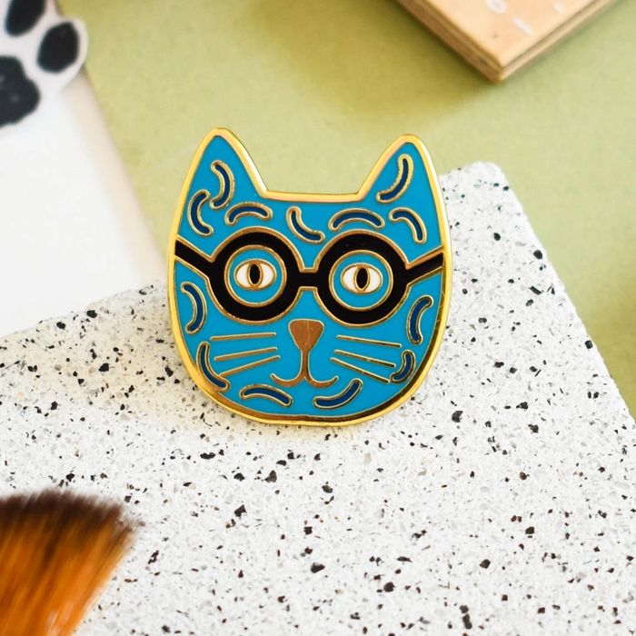 An enamel pin badge with a blue and yellow cat design