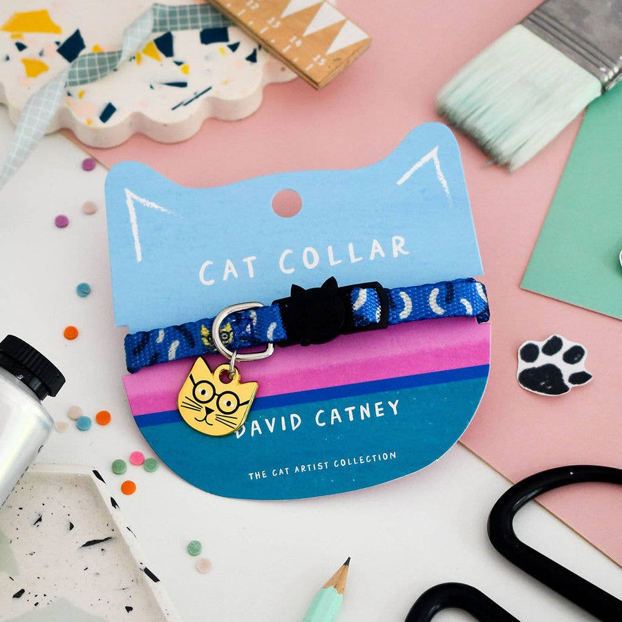 A blue patterned cat collar with a cat-shaped metal tag, displayed on a blue cat-shaped backing card labelled 'DAVID CATNEY'