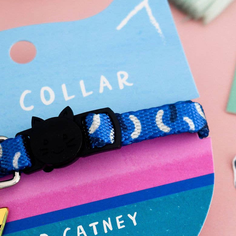 A blue cat collar with white crescent moon and star pattern, featuring a black cat-shaped buckle